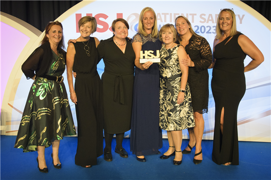 Members of the team are standing on the stage at the event holding up their HSJ Patient Safety Award trophy.