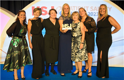 Members of the team are standing on the stage at the event holding up their HSJ Patient Safety Award trophy.