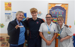 Three nurses stand with teenage Ashby in the middle. The first nurse is wearing two championship medals and holding them in her palm. They are all smiling. 