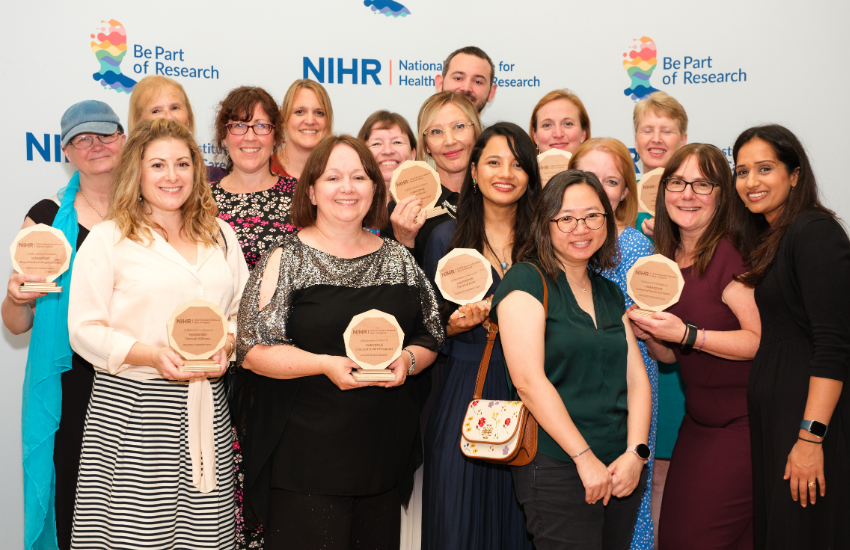 Members of the team are standing together holding their trophies at the awards ceremony. They are standing in front of a screen which has the National Institute for Health and Care Research logo on.