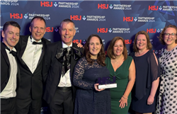 The Innovative Partnership Workforce Solution to Support Endoscopy Training Lists team stood against a HSJ branded blue background holding their Gold Award