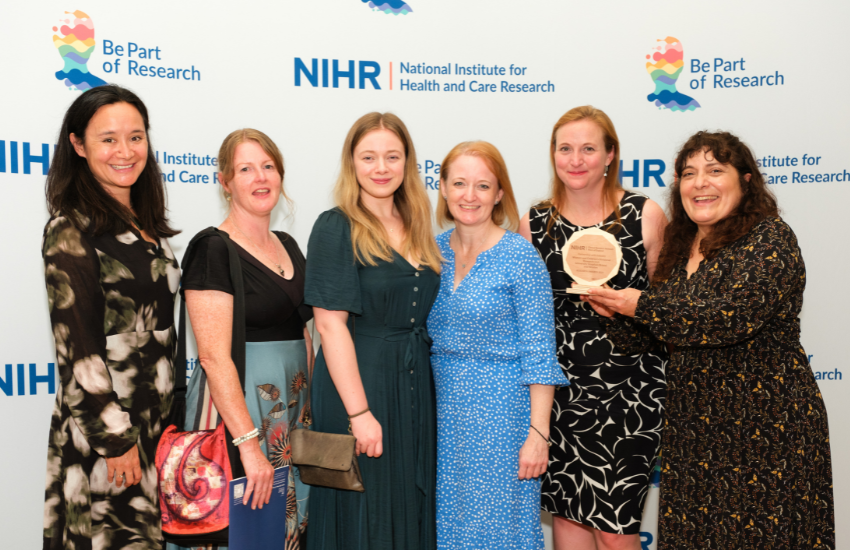 Six members of the team are standing together holding their trophy at the awards ceremony. They are standing in front of a screen which has the National Institute for Health and Care Research logo on.
