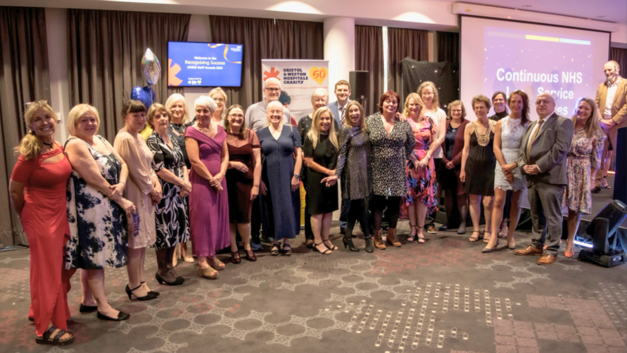 A large group of staff are standing together at the awards ceremony after being recognised for their long service to the NHS.