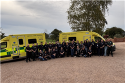 Two ambulances are in the background. In front of them are the Retrieve team all gathered together in their green paramedic uniforms and smiling at the camera